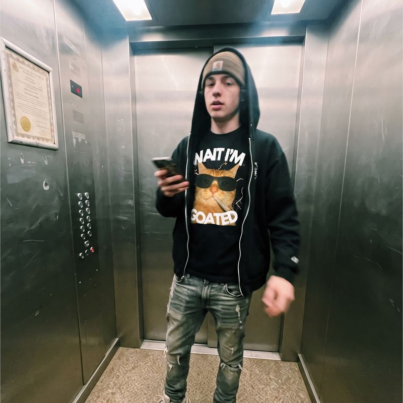 Someone in a lift wearing a hoodie open over the goated tee.
