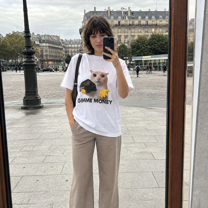 A shop window reflection on a Paris street, wearing the white gimme money tee.